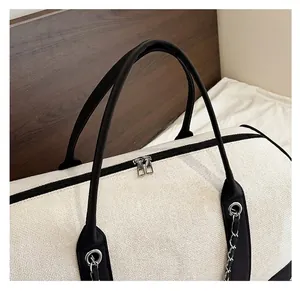 Close-up of canvas travel tote with black leather trim, metal chains and dual zippers