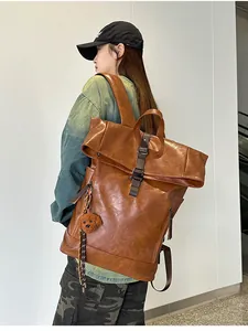 Detail view of large brown vintage leather backpack with roll-top buckle and teddy bear charm