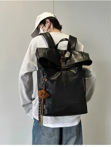 Rear view of model wearing a black leather backpack with roll-top and bear charm