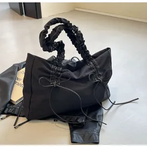 Detail van zwarte shopper met geplooide handgreep en witte strikken op leer oppervlak