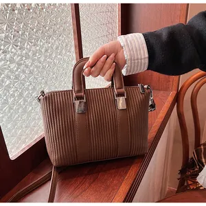 Macro detail of dark brown pleated faux leather tote bag with cylindrical top handles