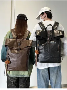 Detail view of waterproof leather roll-top backpacks in brown and black with bear charms