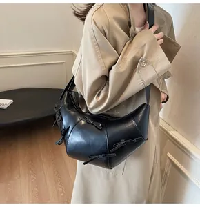 Détail du sac croissant noir avec nœuds porté sur un trench-coat beige élégant