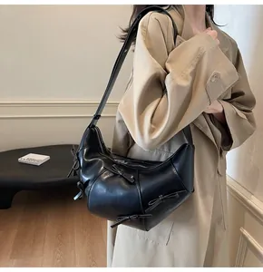 Gros plan détaillé d'un sac bandoulière croissant noir avec nœuds sur manteau beige