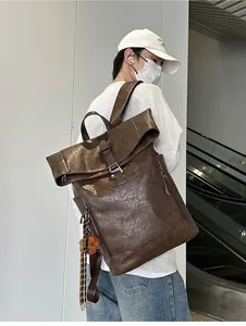 Detail of dark brown leather roll-top backpack with metal buckle and bear charm on model