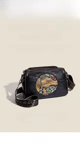 Close-up of black leather bag featuring a gold elephant relief and patterned wide strap