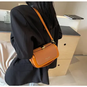 Détail du sac bandoulière orange à boucle dorée porté par un mannequin en costume noir