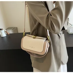 Détail d'un sac bandoulière beige bicolore avec fermoir doré porté sur une veste marron