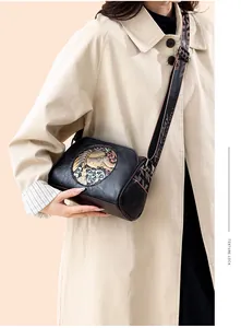 Detail of black cylindrical crossbody bag with colorful elephant relief and wide strap