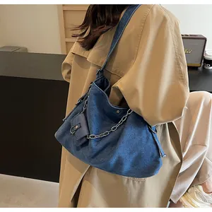 Detail of blue denim tote bag with silver chain and detachable mini pouch on shoulder