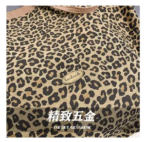 Detail of leopard print fabric underarm bag with a golden handmade metal logo plate