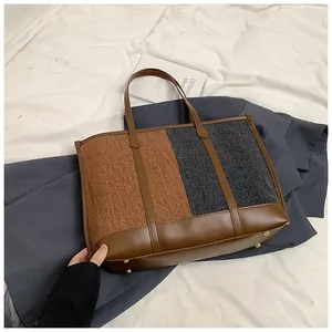 Detail der Kontrast-Tragetasche mit Ledergriffen und schützenden Metallfüßen am Boden