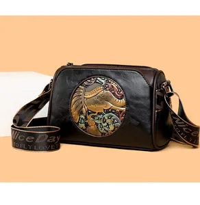 Detail of vintage embossed elephant medallion on black leather bag with wide strap