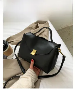Detail of a black matte PU leather handbag with a gold metal clasp on an autumn trench coat