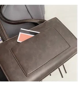 Detail of a dark brown suede shoulder bag featuring a functional front pocket and card slot