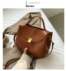 Detail of a brown leather handbag with a gold metal clasp, styled with a blazer and coffee