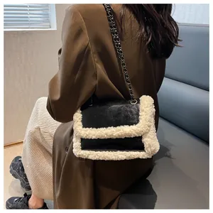 Detail of black leather shoulder bag with plush beige trim and metal chain strap on model