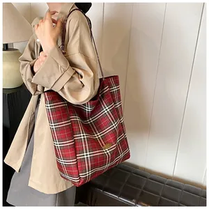 Detailed side view of large red plaid tote bag with golden metal logo plaque on model