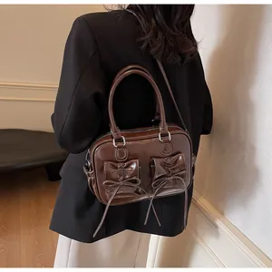 Deep brown glossy handbag with bow pockets and contrast stitching shown on model