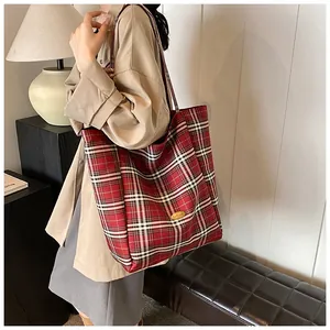 Detail of red plaid tote bag featuring golden metal logo and premium leather shoulder strap