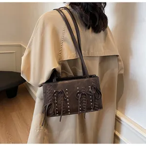 Detail of a dark brown suede underarm bag with silver rivets and ribbon accents