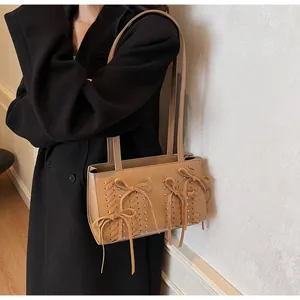 Close-up of khaki suede shoulder bag with bow details and metal studs on a black coat