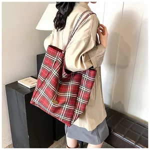 Detailed view of red plaid tote bag with metallic logo plate on model in casual setting