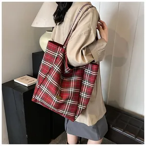 Detail showing red tartan plaid canvas tote bag with metal emblem on wide shoulder strap