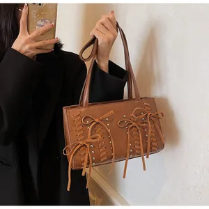 Caramel suede shoulder bag featuring woven bow details and silver studs on a model