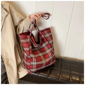 Detail of red tartan plaid tote bag with golden metal logo and thick fabric texture