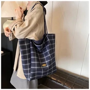 Detail of blue plaid tote bag featuring a golden metal nameplate and canvas texture