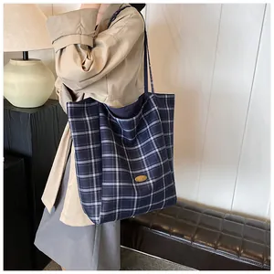 Detailed close-up of dark blue plaid canvas tote bag with elegant golden metal logo plaque