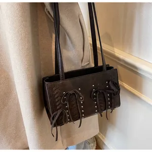 Close-up of brown suede shoulder bag with silver rivets and bow tie detail