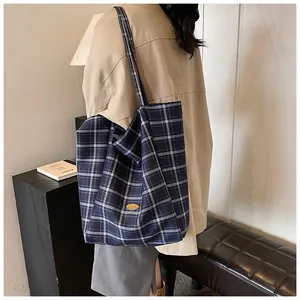 Detail of navy blue plaid canvas tote bag with long shoulder strap and golden logo plate