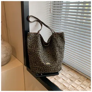 Detail of leopard print canvas tote bag featuring an oval metal logo and brown shoulder straps