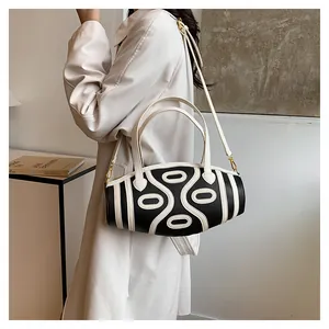Detail of a black and white striped cylindrical bucket bag with gold hardware and strap