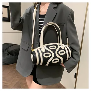 Detail of a black and white cylinder bucket bag in pebbled leather worn by a model