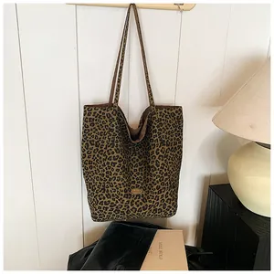 Detail of leopard print tote bag with metal emblem hanging on a white wooden wall