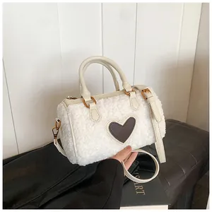 Detailopname van een witte pluche handtas met hartvormige patch en gouden metalen sluitingen