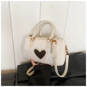 Close-up van witte pluchen handtas met lederen hartpatch en gouden metalen details