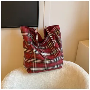 Macro shot of red plaid canvas tote bag showing textured fabric and central oval logo detail
