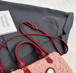 Detail van de roze pluche handtas met bordeauxrode lederen handvatten en gouden gespen
