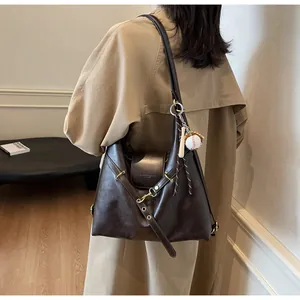 Detalle de bolso tote de cuero marrón oscuro con hebillas y colgante de béisbol