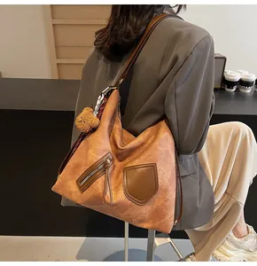 Detail of vintage brown leather tote bag with plush bear charm and printed scarf accessory