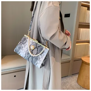 Détail du sac à main serpent avec anse en perles et fermoir doré sur un manteau beige