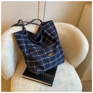 Detail of blue checkered canvas tote bag with metal logo on a plush white chair