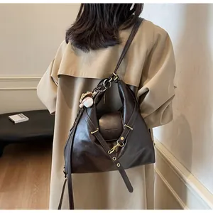 Detalle de bolso bandolera grande en cuero marrón oscuro con ganchos metálicos mate