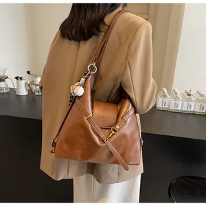 Bolso hobo marrón de cuero sintético con colgante de béisbol usado por una modelo de espalda