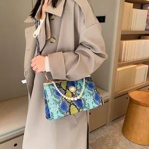 Sac à main chic motif serpent avec chaîne en perles porté par un mannequin en trench-coat