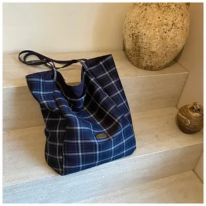 Detail of blue and white plaid canvas tote bag showing handmade label on stone steps